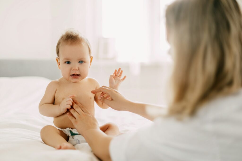 A young mother smears the baby's tummy with baby cream. Child care, childhood, parenting
