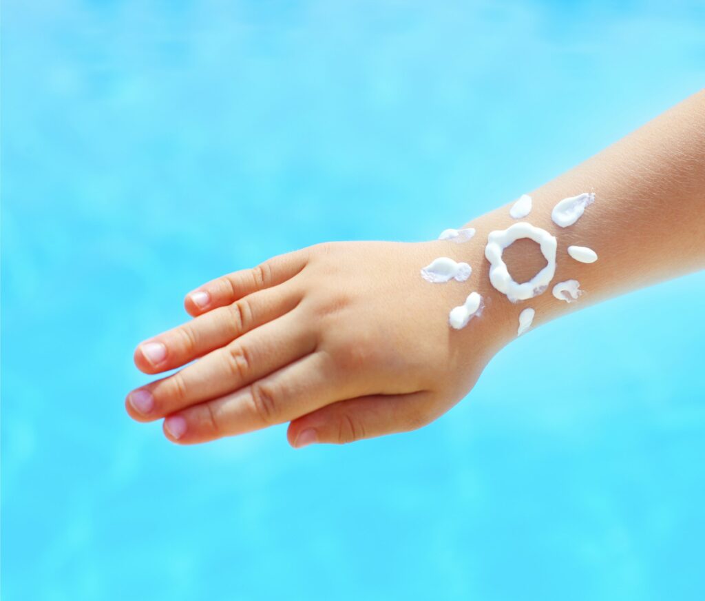 Little hand of the baby with suntan lotion near the pool