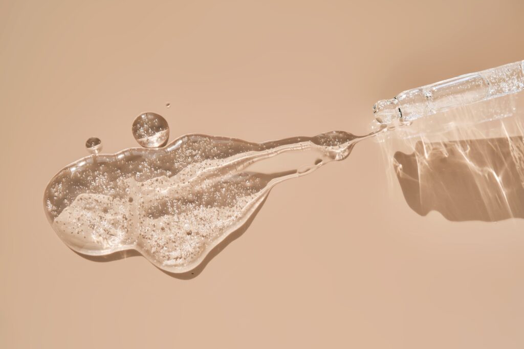 Pipette with cosmetic hyaluronic anti-aging serum on a dusty pink background.