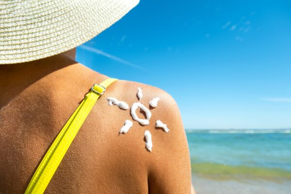 Back view of young woman tanning at the beach with sunscreen cream in sun shape