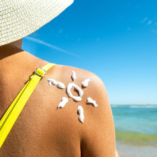 Back view of young woman tanning at the beach with sunscreen cream in sun shape